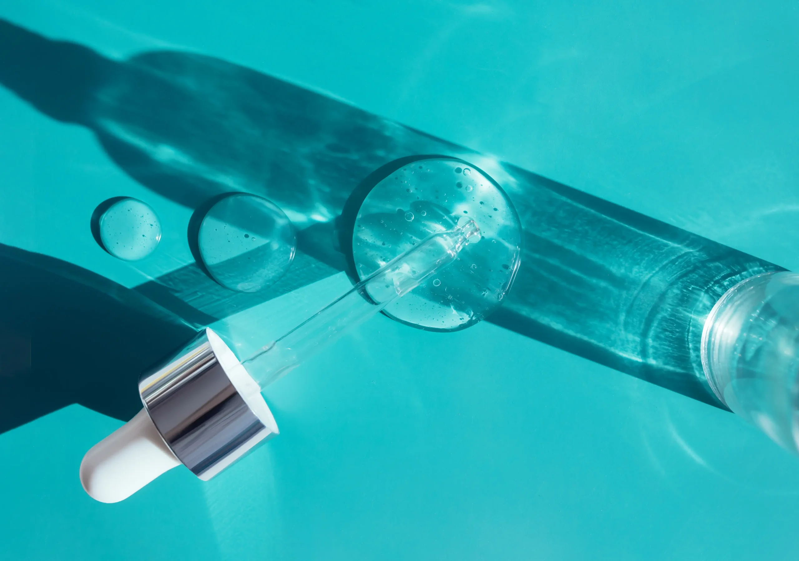 Abstract image with a dropper bottle and liquid drops on a clean, vibrant turquoise surface, subtly representing advanced oral hygiene solutions and modern techniques used for effective teeth cleaning in Abu Dhabi.